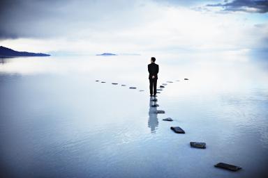 Businessman at fork of stone pathway in water